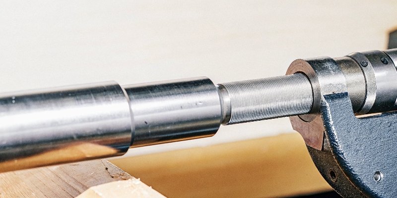 A close-up shot of a micrometer precisely measuring a freshly ground, shiny metal shaft