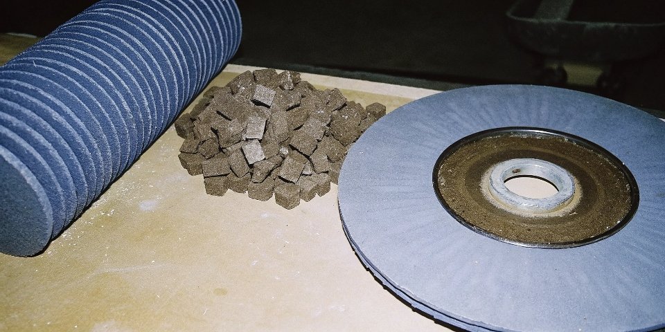 A pile of brown fused alumina abrasive grains next to a finished grinding wheel.