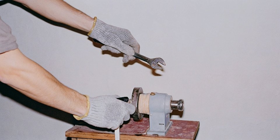 A person wearing safety gloves using a wrench to loosen the nut on a bench grinder.
