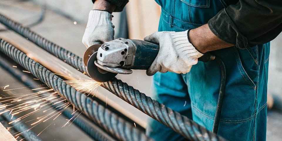 A worker using a 4.5-inch angle grinder to cut metal rebar.
