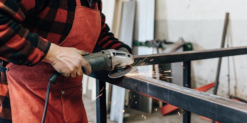 A worker using a small angle grinder on a metal piece