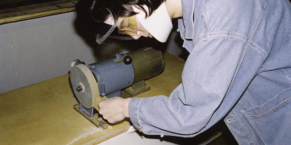 A person wearing safety glasses and a face shield inspecting the tool rest on a bench grinder.