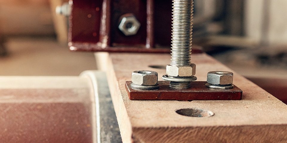 A close-up view of a bolt with washers and a nut securing a bench grinder's base to a workbench.