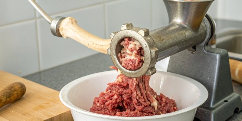 A meat grinder with a large bone visibly stuck in the feeding mechanism